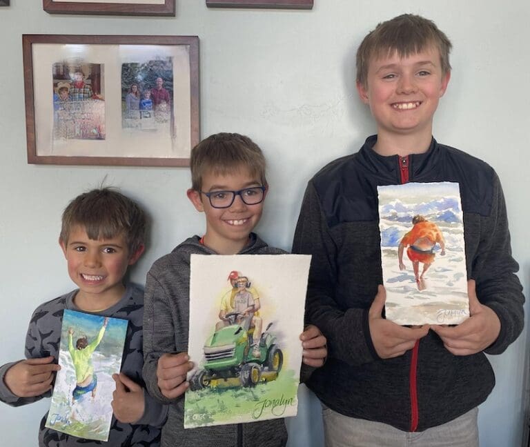Three boys holding their watercolor paintings of themselves.