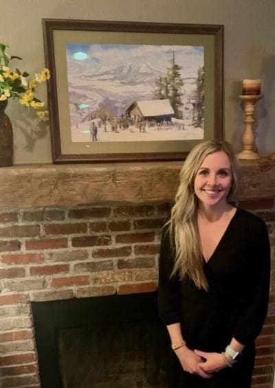 Rachel Fritzler standing next to her anniversary present, a commissioned art piece of her first date with her husband on top of the Steamboat ski mountain.